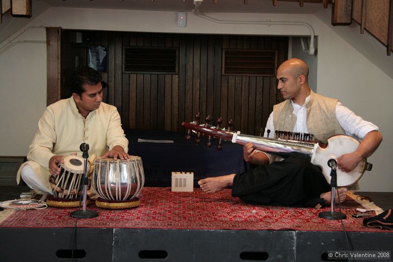 Udit Pankhania (left, playing Table) and Tarun Jasani (right, playing Sarod) at Walton Church, The Open University, 25-Jun-2008.\n\nThe body of the Sarod is of course hollow and has a top layer of goat skin; the bridge is made from bone and because of the use of metal strings, wears down with time.\n\nThe box in the middle at the back is an electronic drone; being electronic, its pitch doesn't drift in different conditions, meaning the two players have something they can tune to. Its sound would traditionally be played by another musician on a Tambura.