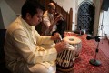 Udit Pankhania tunes his Tabla. The skin is tensioned by a number of cords that run down the sides; inside each pair of cords is a large wooden toggle. The further down the barrel of the drum the toggle is moved, the tighter the skin is made, raising the pitch.\n\nThe black circles in the middle of each drum skin, which enable an even wider variety of sounds to be made, are built up in layers of rice starch mixed with coal dust.